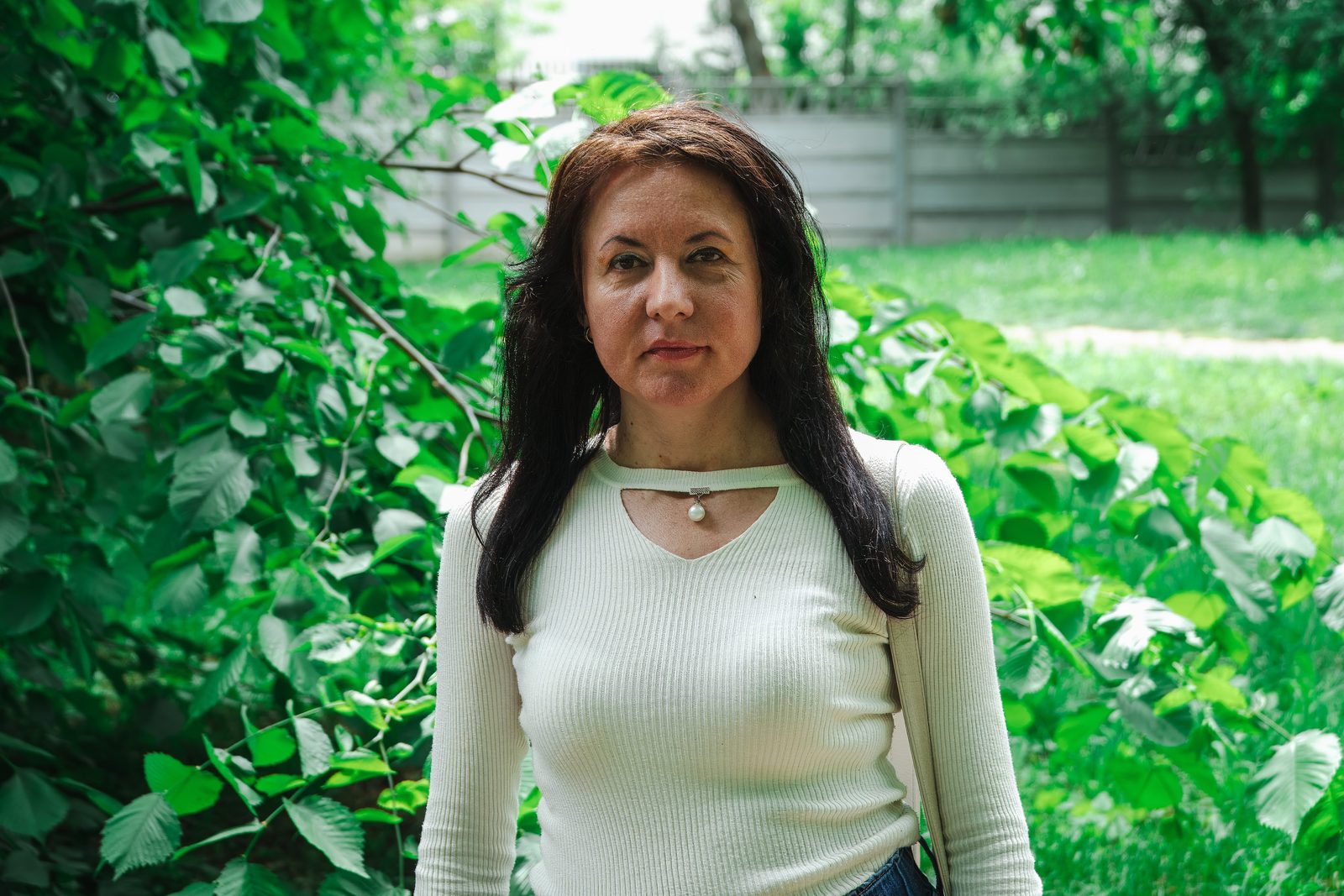 Portret în fața frunzișului verde, bluză albă cu perlă